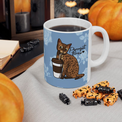Mug with a Bengal cat drinking from a coffee cup and 'Purrrfect Brew' text on a blue floral patterned background.