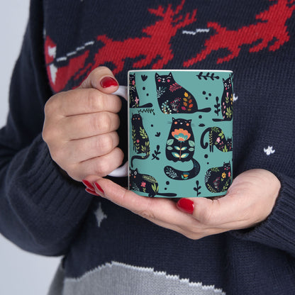 Mug with black cats and floral pattern on a blue background.