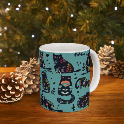 Mug with black cats and floral pattern on a blue background.