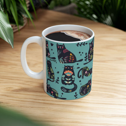 Mug with black cats and floral pattern on a blue background.