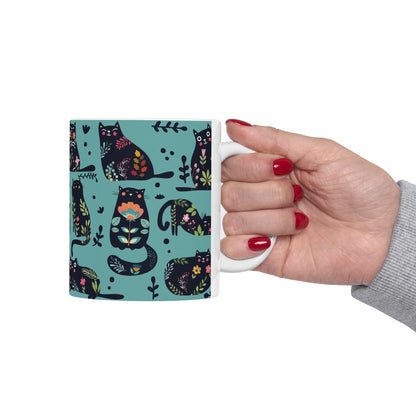 Mug with black cats and floral pattern on a blue background.