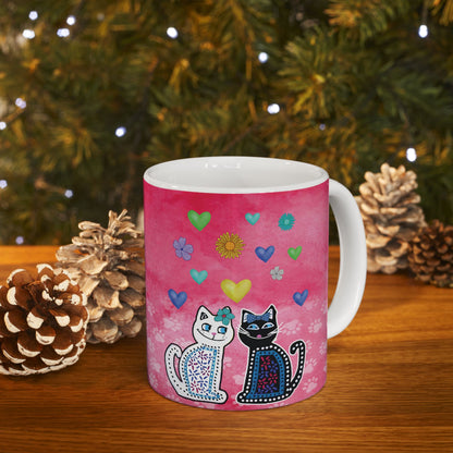 Mug with two cats and colorful hearts and flowers design on a pink background.