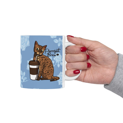 Mug with a Bengal cat drinking from a coffee cup and 'Purrrfect Brew' text on a blue floral patterned background.