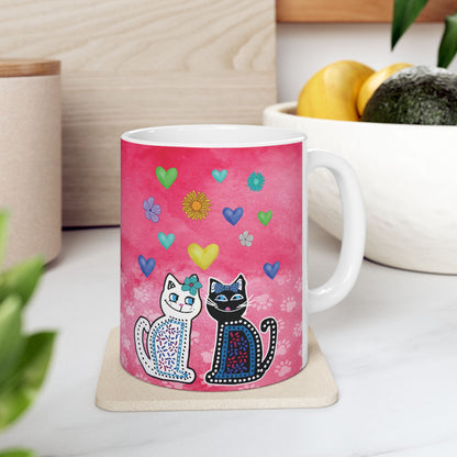Mug with two cats and colorful hearts and flowers design on a pink background.