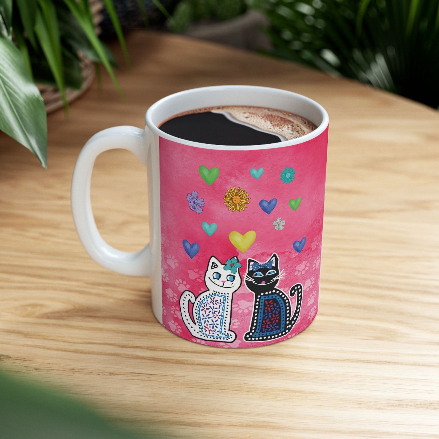 Mug with two cats and colorful hearts and flowers design on a pink background.