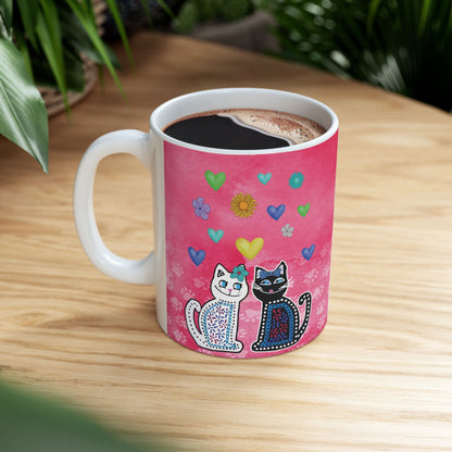 Mug with two cats and colorful hearts and flowers design on a pink background.