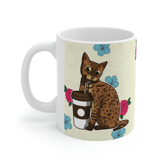 Cream mug of a cartoon Bengal cat drinking from a cup against a floral background